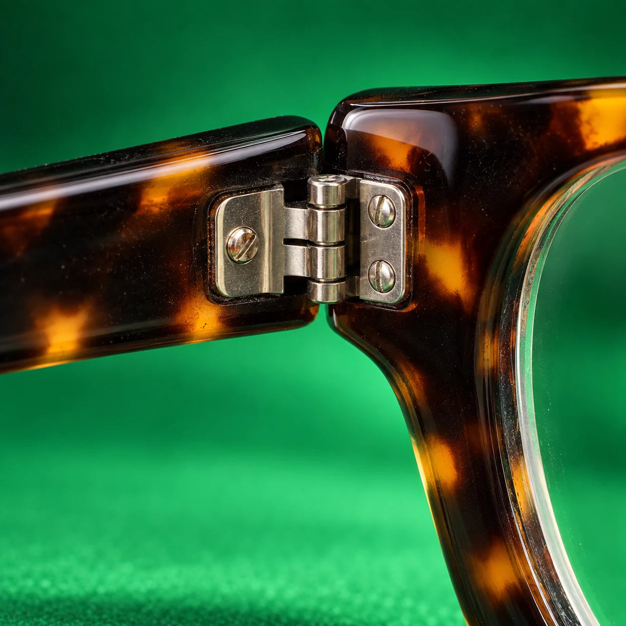 Realistic macro photograph of a tortoiseshell eyeglass hinge, screws, and narrow grooves