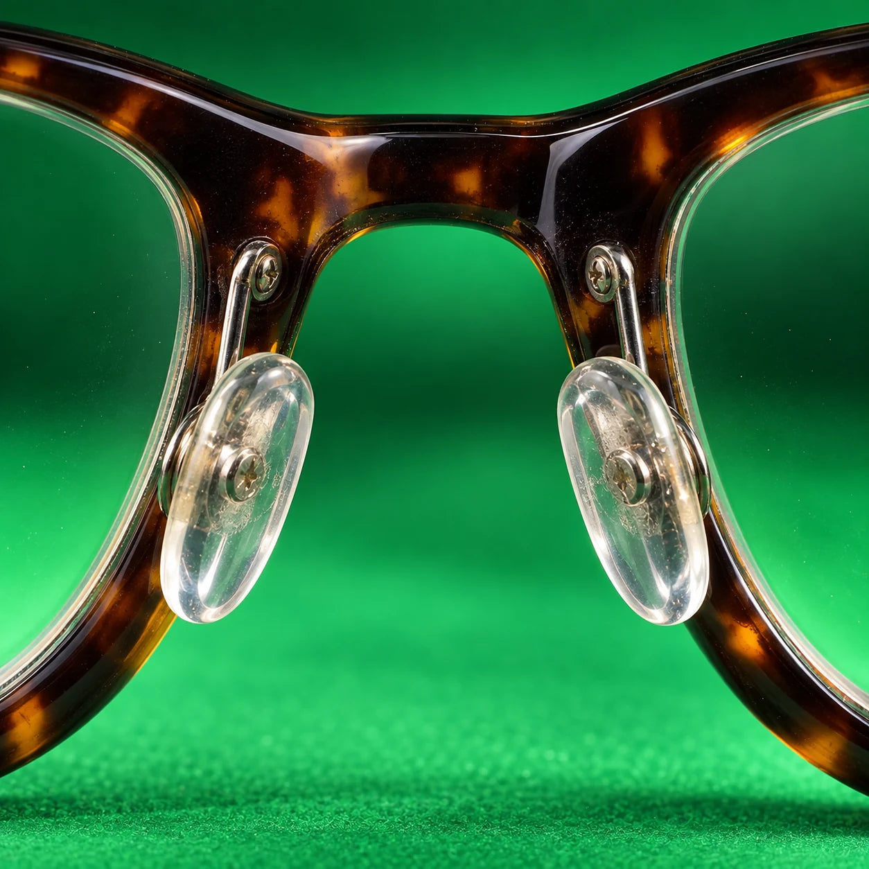 Realistic macro photograph of two transparent eyeglass nose pads and their metal supports