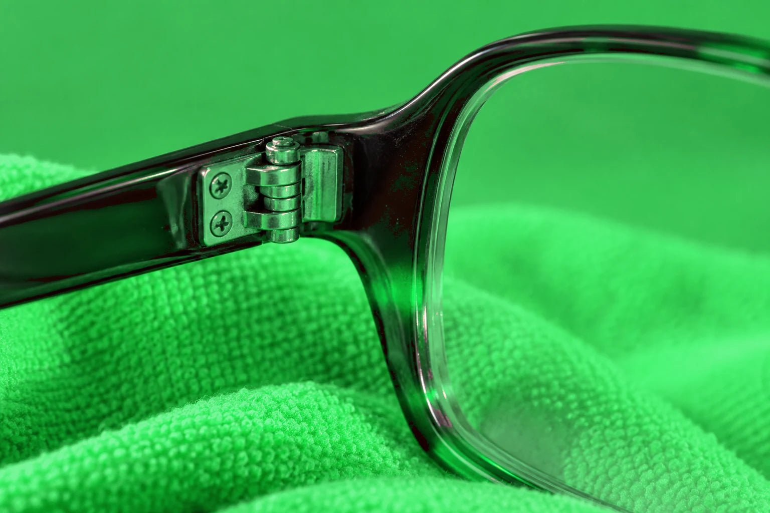 Illustrative close-up of an eyeglass hinge and lens edge on green cloth