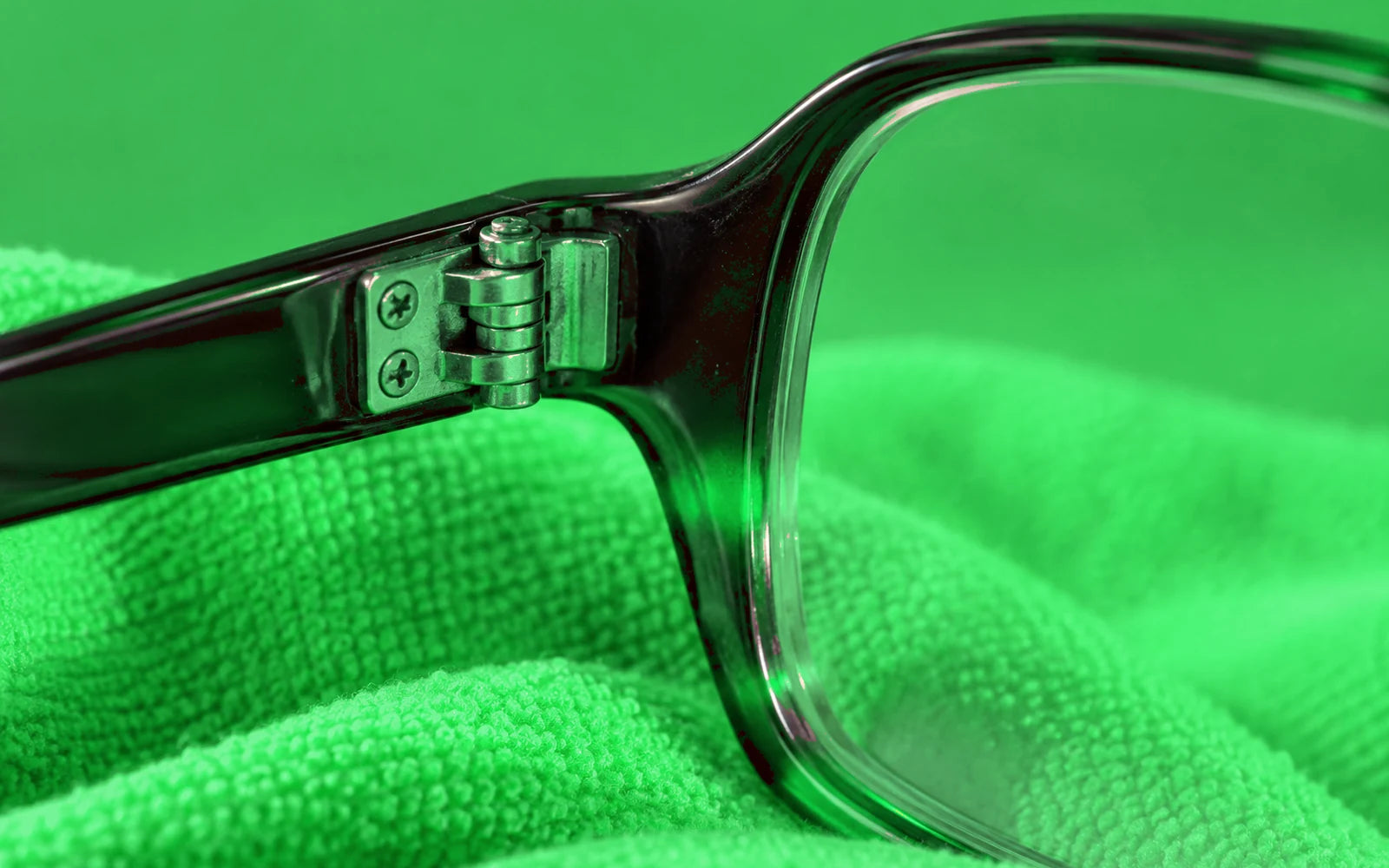 Illustrative close-up of an eyeglass hinge and lens edge on green cloth